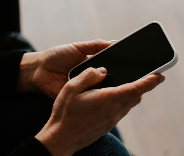 Person holding a smartphone in hands, reflecting on wedding invitation regrets involving groom's grandfather stroke incident. - 14