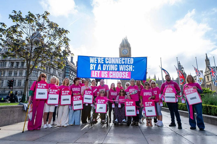 Support group wearing pink shirts holds signs and banner advocating choice after woman ended life by starving.