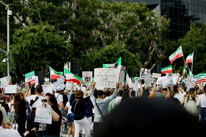 Crowd holding signs and flags protesting a resurfaced case of 17YO mom brutally assassinated by husband, sparking public anger.