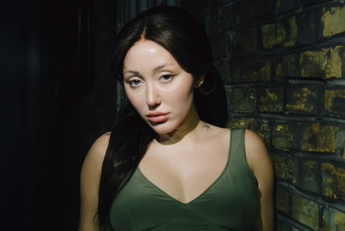 Noah Cyrus posing in a green top against a brick wall, showcasing a dramatic transformation amid plastic surgery rumors. Noah Cyrus posing in a green top against a brick wall, showcasing a dramatic transformation amid plastic surgery rumors.