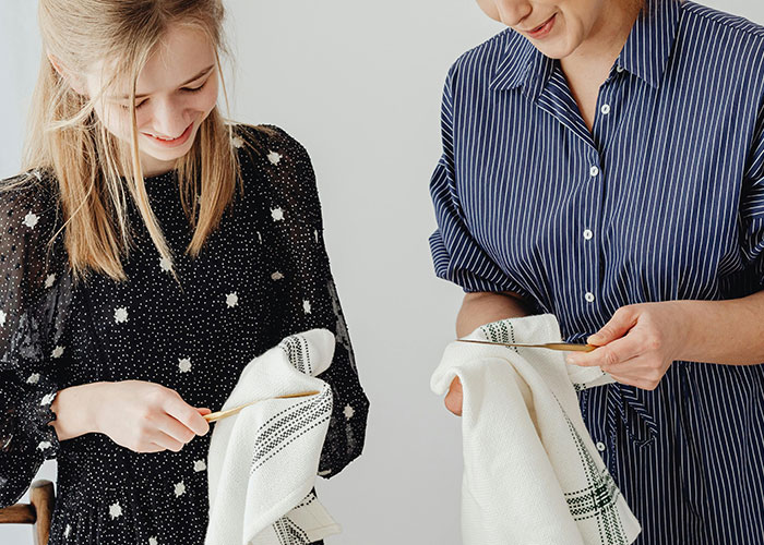 Two women smiling while drying dishes together, illustrating bizarre family habits people thought were normal.