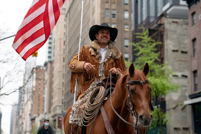 Man in fringed jacket and black hat riding horse in city, illustrating people facing consequences of their own stupidity.