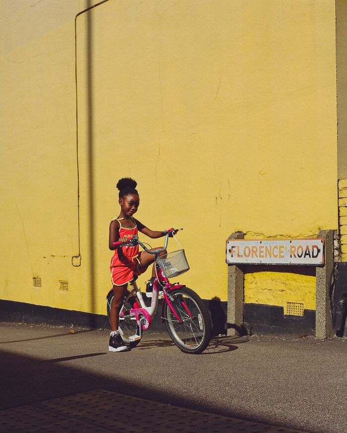 Young girl in a red outfit with a pink bike posing on a sunny day on a street in London, capturing honest street photography.