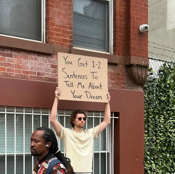 Man holding sign in urban setting with message about sharing a dream, representing Dude With The Sign humor and thoughts.