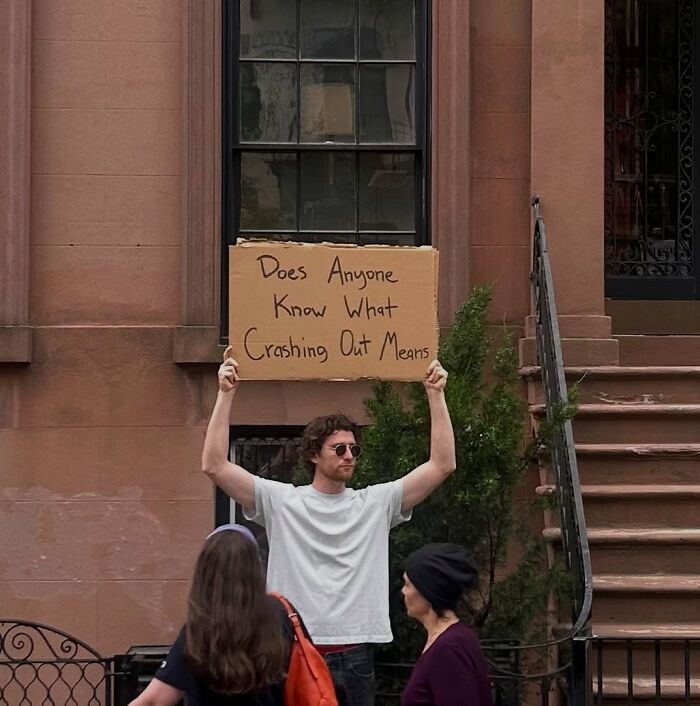 Man holding a sign with a message standing on a city sidewalk representing dude with the sign humor and thoughts