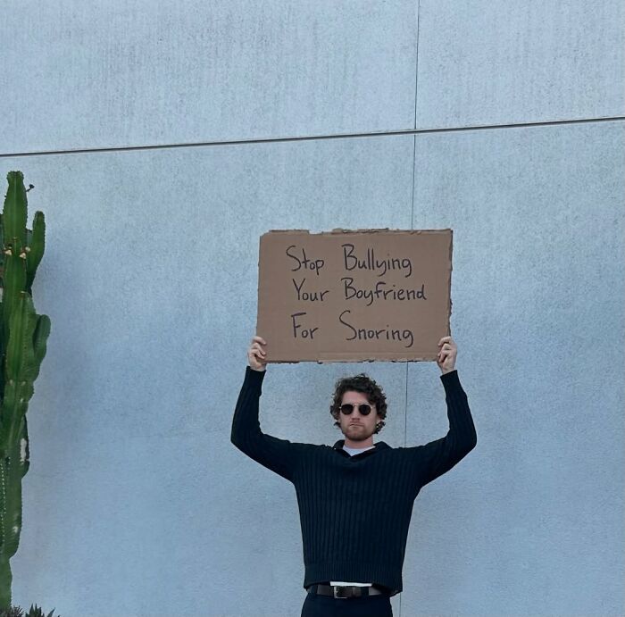 Man holding sign that reads stop bullying your boyfriend for snoring in a dude with the sign photo.