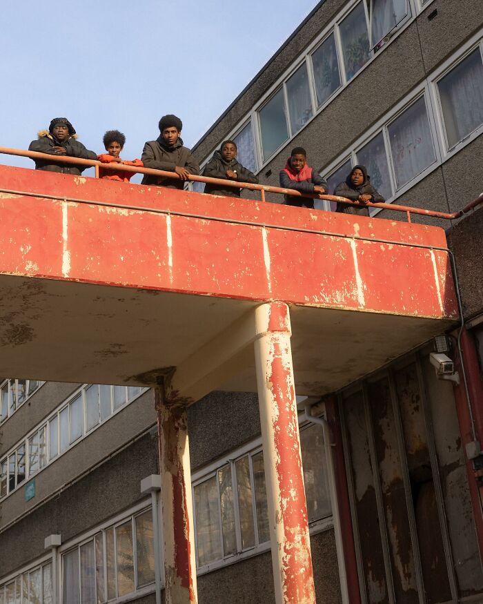 Group of young people leaning on a weathered balcony railing in a London housing estate street photography by Nico Froehlich.