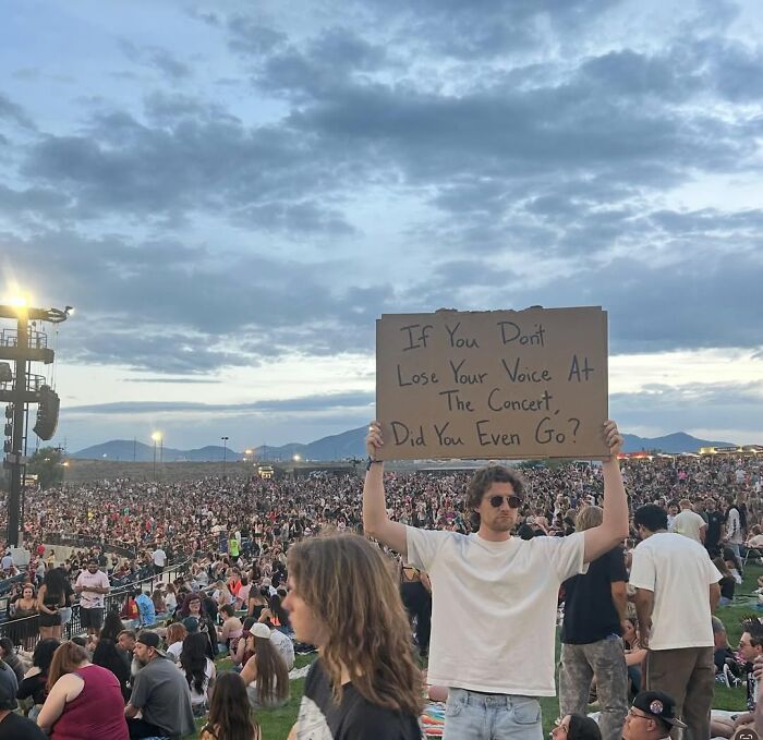Man at crowded outdoor concert holding sign with message, representing dude with the sign capturing unspoken thoughts.