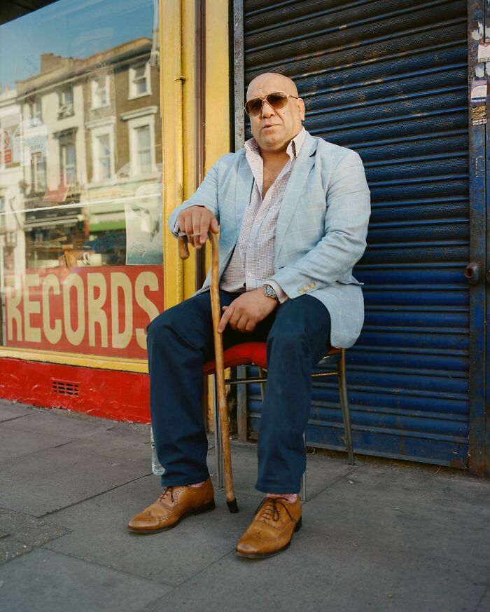 Man with cane wearing sunglasses and blazer sitting on a chair outside a record store in London streets photography.