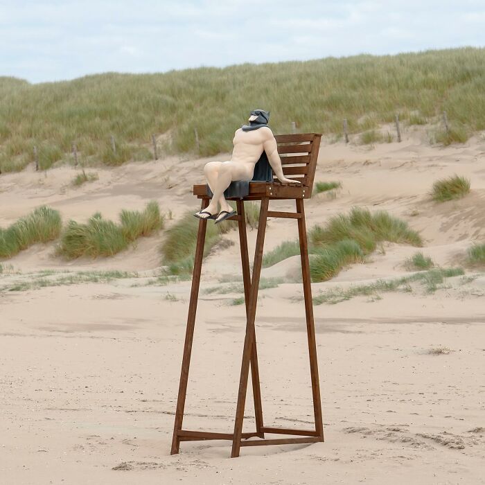 Large wooden chair in public space with n**e superhero figure wearing mask and cape relaxing outdoors in street art display.