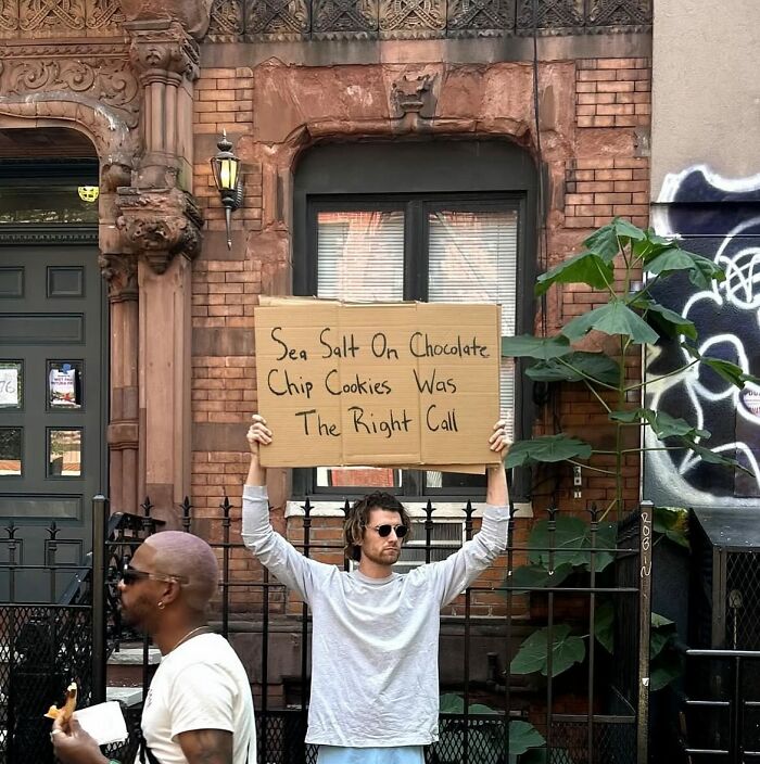 Man holding a cardboard sign about sea salt on chocolate chip cookies, representing Dude With The Sign humor and thoughts.