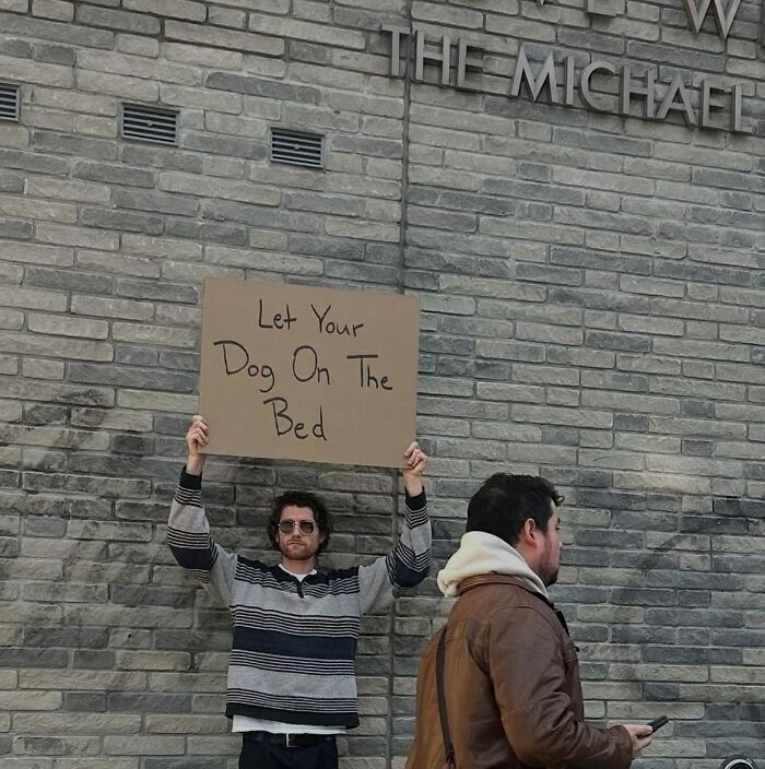 Man holding a sign saying let your dog on the bed, representing dude with the sign expressing common thoughts.