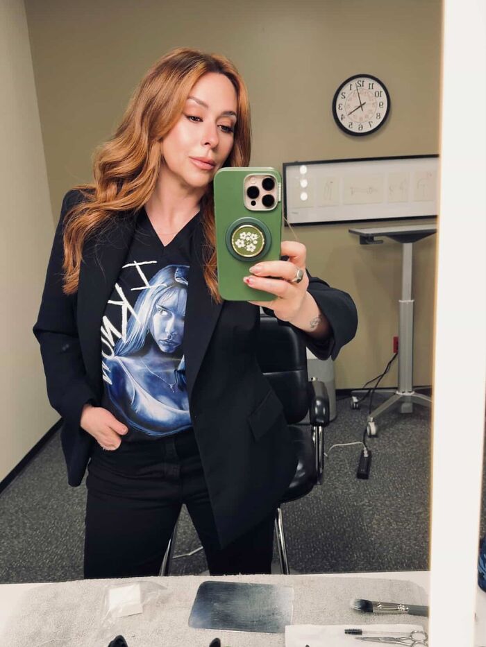 Jennifer Love Hewitt taking a mirror selfie wearing a black blazer and graphic shirt after premiere, fans defend against body shaming.