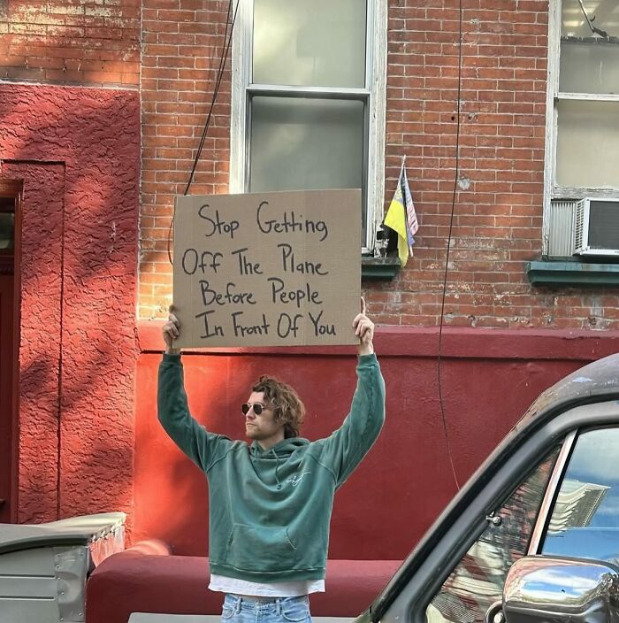 Man holding a cardboard sign with a witty message standing outside a brick building in dude with the sign style