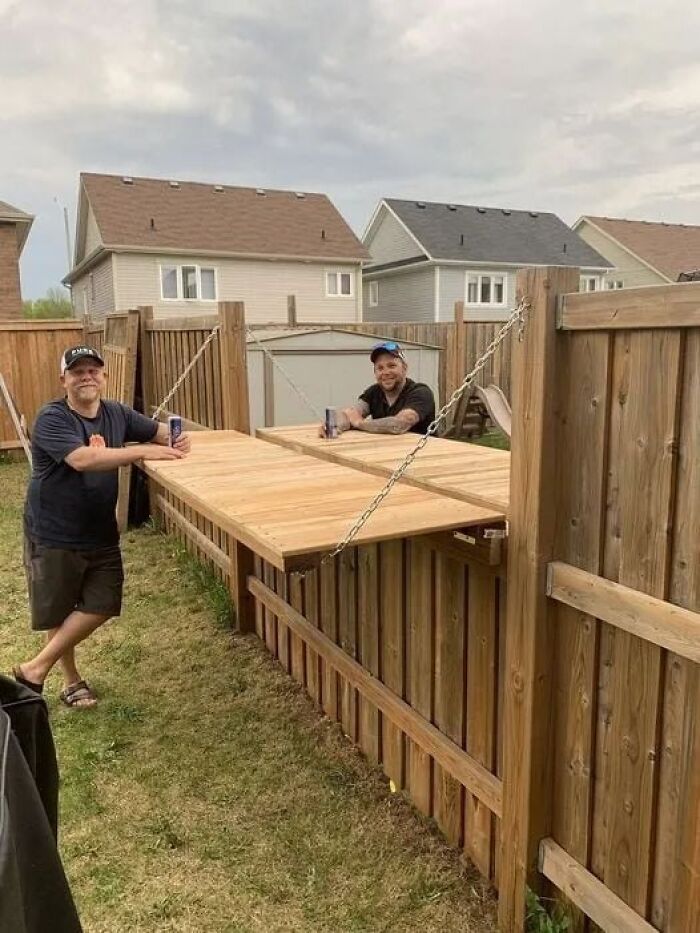 Two men enjoying drinks with a wooden fold-out table on a backyard fence, showcasing the beauty of planet earth.