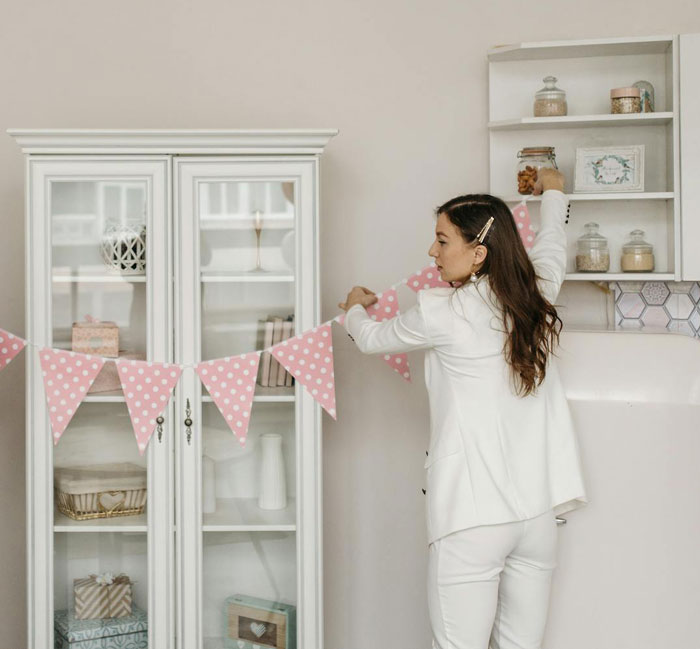 Mom hanging pink polka dot banners in kitchen preparing for menstruation celebration for 12-year-old daughter. - 6