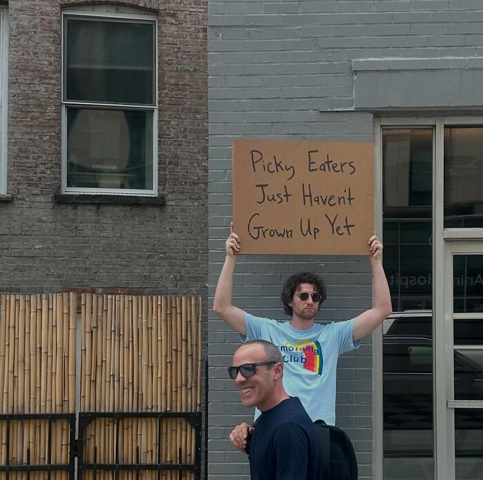 Man holding a sign saying picky eaters just haven't grown up yet, representing Dude With The Sign humor and sarcasm outdoors.