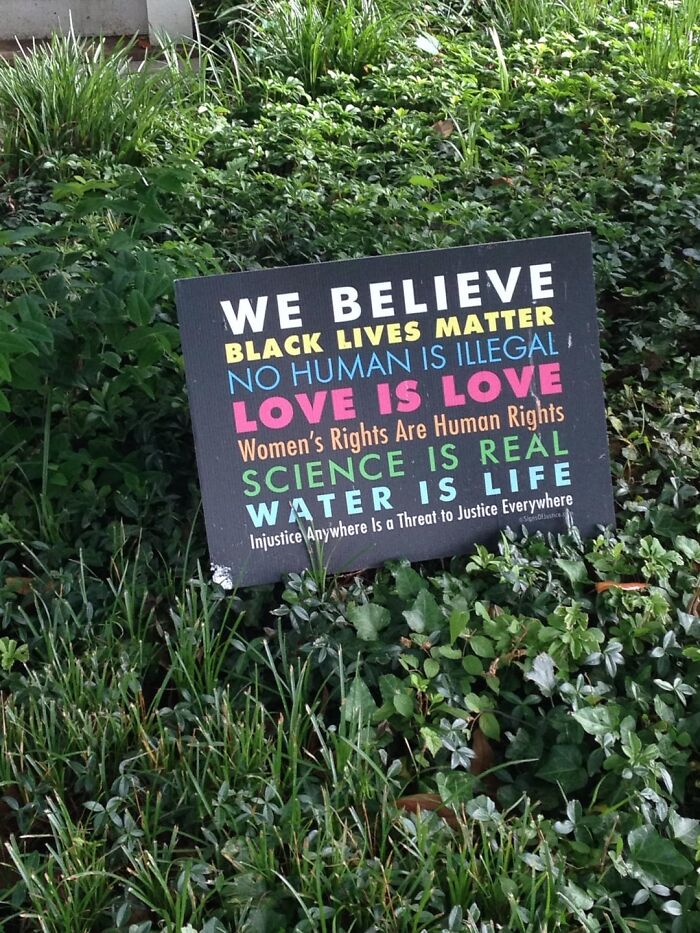 Sign with messages about love, science, water, and human rights placed in green plants showcasing the beauty of planet Earth.