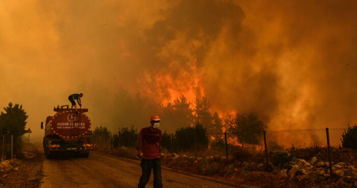 Firefighter wearing mask near a burning forest with smoke and flames during catastrophic wildfire in recent history.