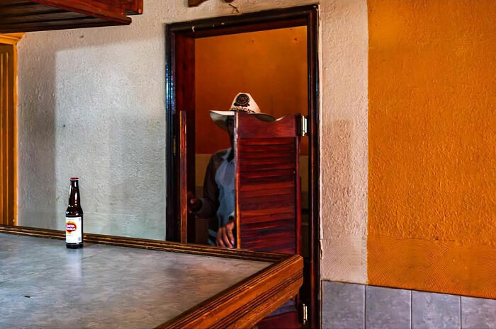 Man wearing a hat entering through a half-open door in a colorful street scene capturing honest street moments.