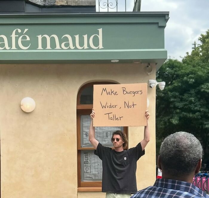 Man holding a sign saying make burgers wider not taller, part of Dude With The Sign viral messages series outdoors.