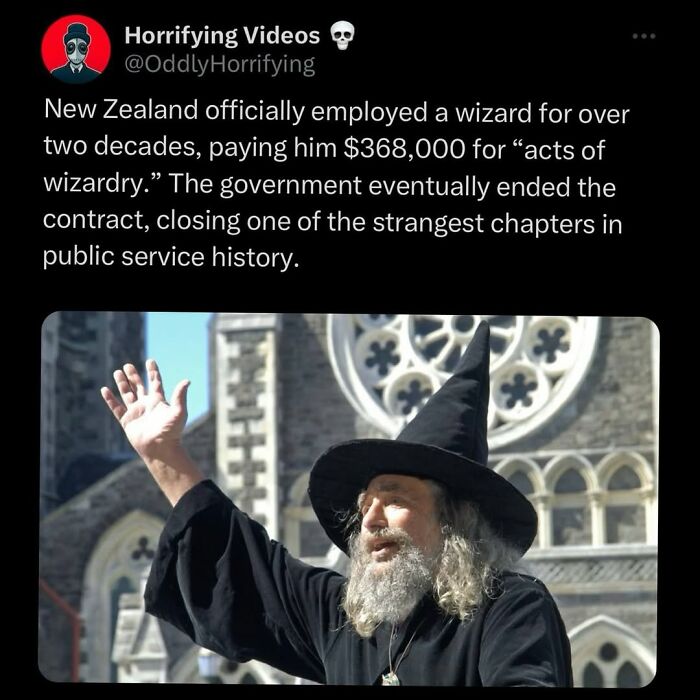 Man dressed as a wizard raising his hand in front of a gothic building, an odd and unnerving image from horror videos.