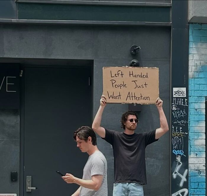 Man holding a cardboard sign about left-handed people in a city street, representing Dude With The Sign humor and messages.