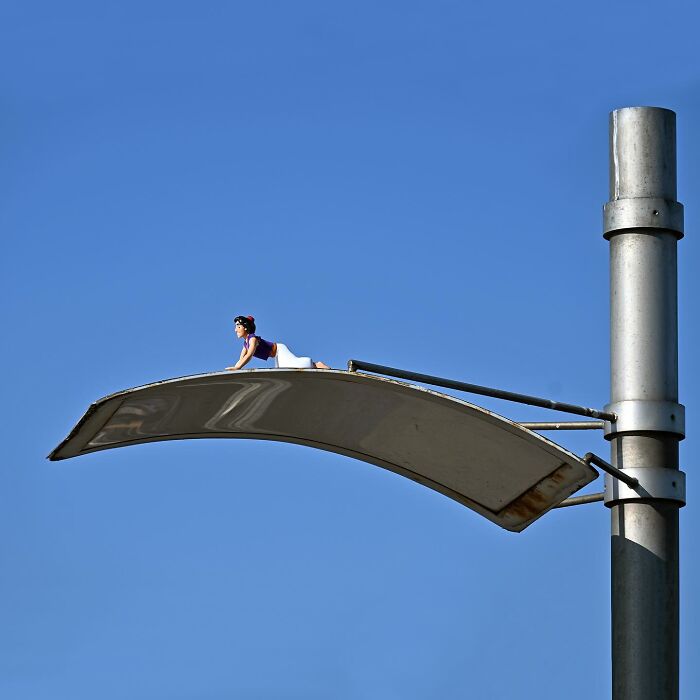 Miniature figure of a character crawling on a curved metal surface showcasing clever street art in public spaces by Frankey.