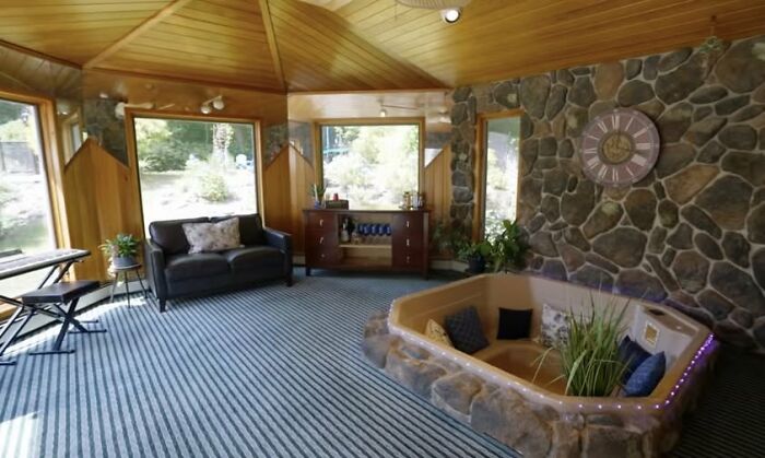 A home interior with a sunken seating area surrounded by stone, striped carpet, and wooden panel ceiling highlighting creative home design fails.