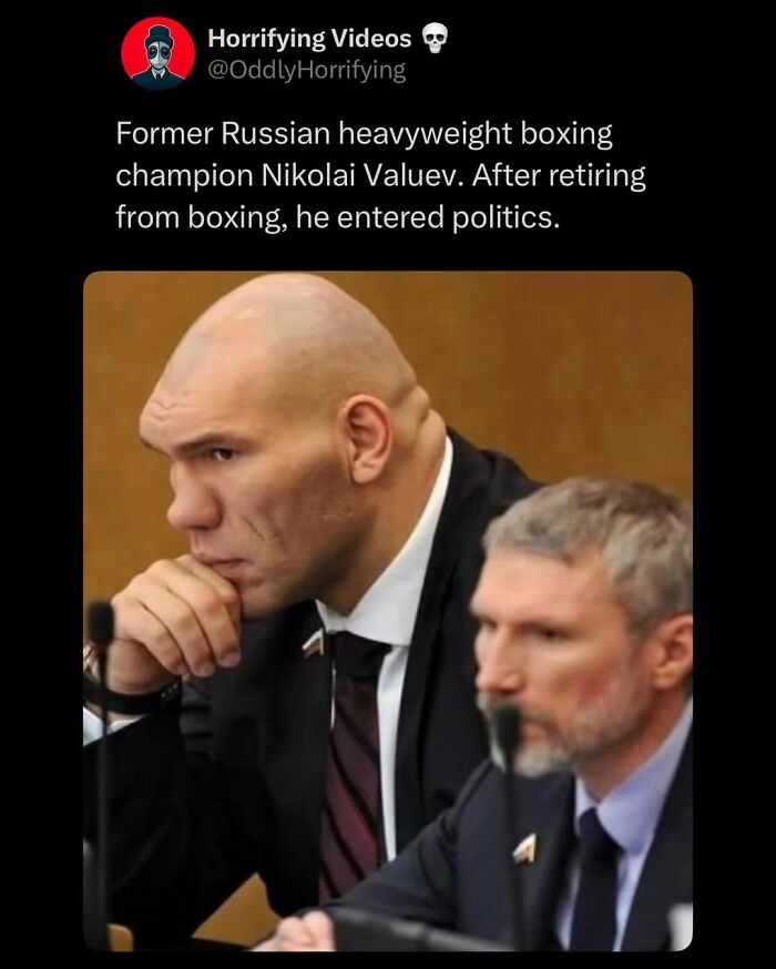 Former Russian heavyweight boxer Nikolai Valuev in a suit, seated at a political meeting, reflecting a strangely unnerving image.