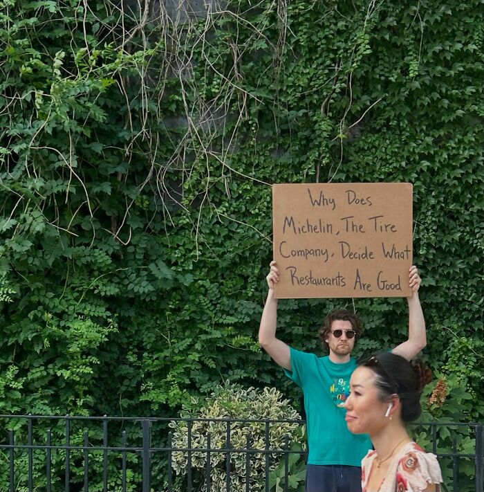 Man known as Dude With The Sign holding a cardboard sign with message about Michelin and restaurants outdoors
