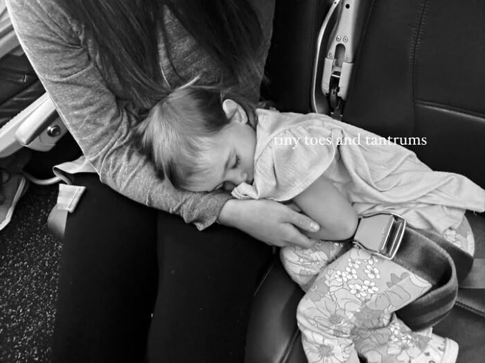 Mother comforting toddler asleep on airplane seat, illustrating a public flight experience with toddler tantrums and chaos.