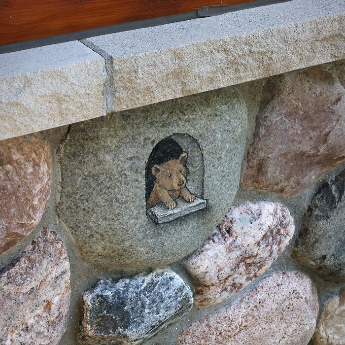 Small chalk drawing of a bear cub peeking through a tiny window in a stone wall, inspired by David Zinn sidewalk art.