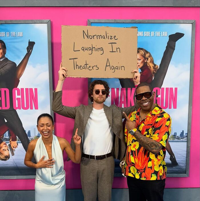 Dude With The Sign holding a cardboard message about normalizing laughing in theaters again with two people posing happily