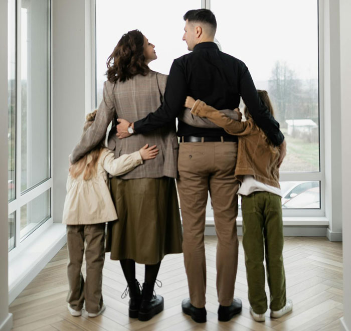 Family of four embracing near large windows, symbolizing support and a menstruation celebration for a 12-year-old daughter. - 51