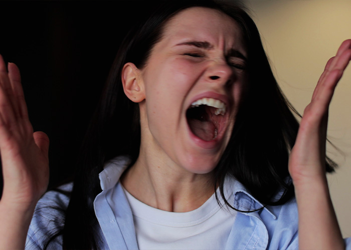 Woman with long dark hair frustrated and yelling indoors, expressing distress triggered by roommate&rsquo;s Jewish traditions and OCD.