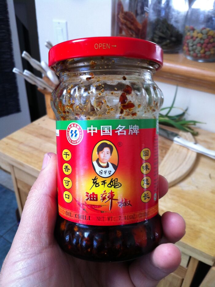 Hand holding a jar of Chinese oil chili sauce in a kitchen setting, symbolizing a from poverty to super wealthy story.