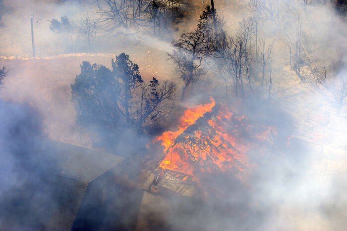 House engulfed in flames amid dense smoke and burning trees during one of the most catastrophic wildfires in recent history.