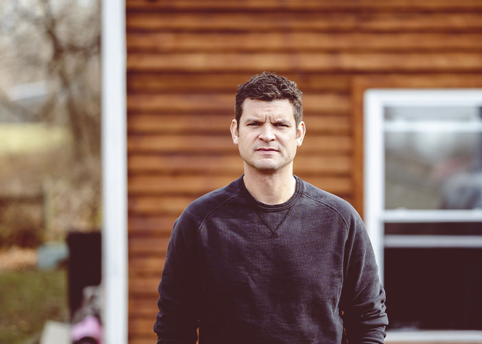 Man standing outside a house, looking serious, representing tension in a relationship after a red-flag argument.
