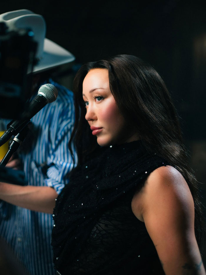 Noah Cyrus wearing a black outfit near a microphone with a soft focus on her dramatic transformation and plastic surgery rumors. Noah Cyrus wearing a black outfit near a microphone with a soft focus on her dramatic transformation and plastic surgery rumors.