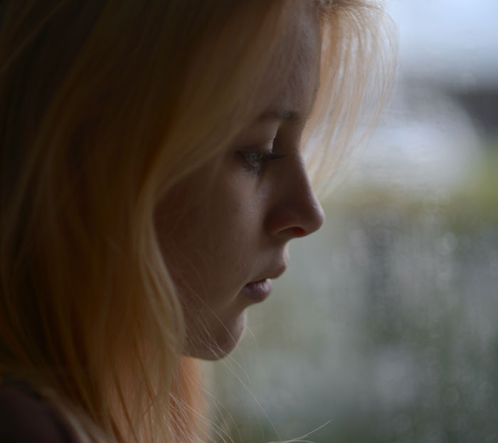 Profile of a thoughtful girl reflecting by a window after surviving cancer and accepting her prosthetic leg.