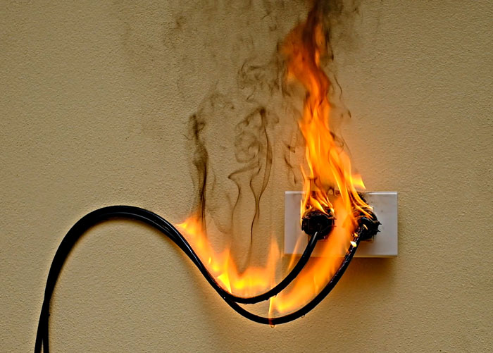 Electrical outlet fire caused by faulty wires burning on a beige wall, illustrating safety tips to stay safe and alive.