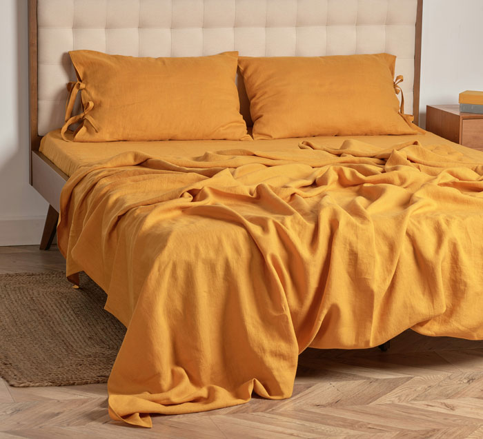 Bed with mustard yellow bedding and pillows in a modern bedroom highlighting oldschool home trends millennials are over
