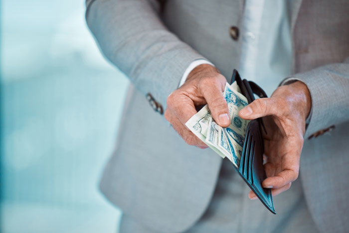 Man in gray suit holding a wallet and counting money, illustrating unexpected things people learned about the rich.