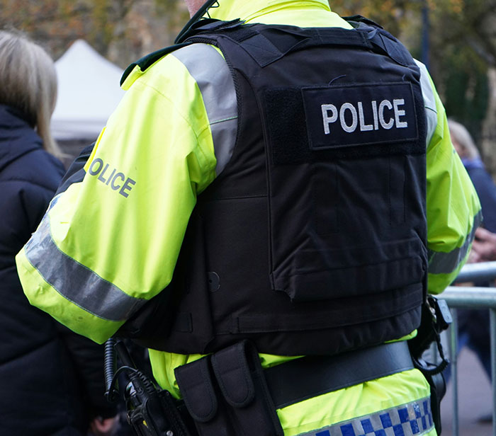 Police officer in high-visibility jacket and vest monitoring neighborhood at night amid reports of mysterious cat-suit figure.