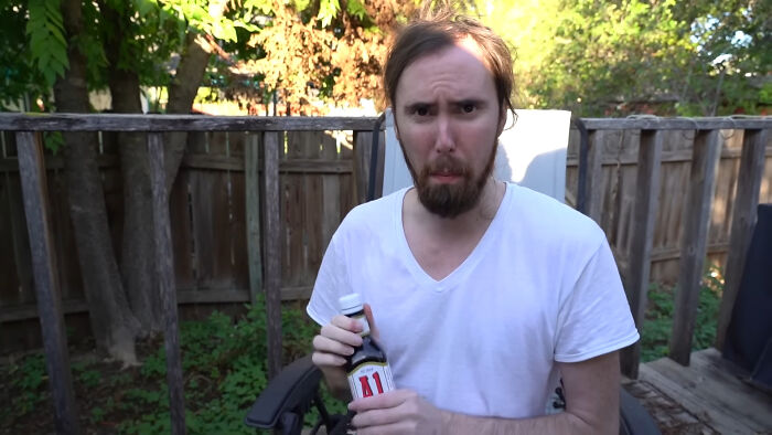 Man in a white shirt holding a bottle outdoors with a surprised expression in a people share unsubscribed YouTubers context.