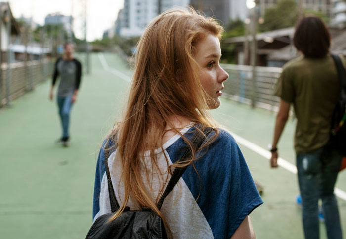 Young woman with red hair walking in public space, highlighting women sharing inappropriate comments from men.
