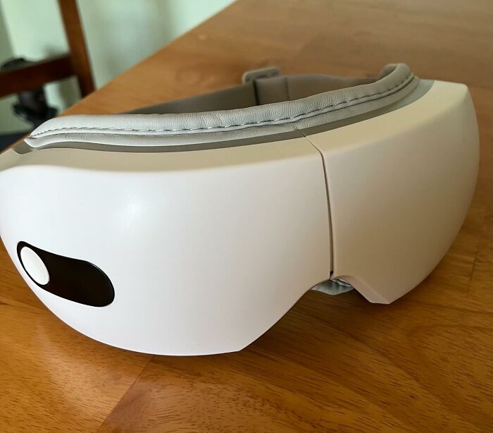 White wearable eye massager device on a wooden table, a genuinely cool gift idea for relaxation and stress relief.