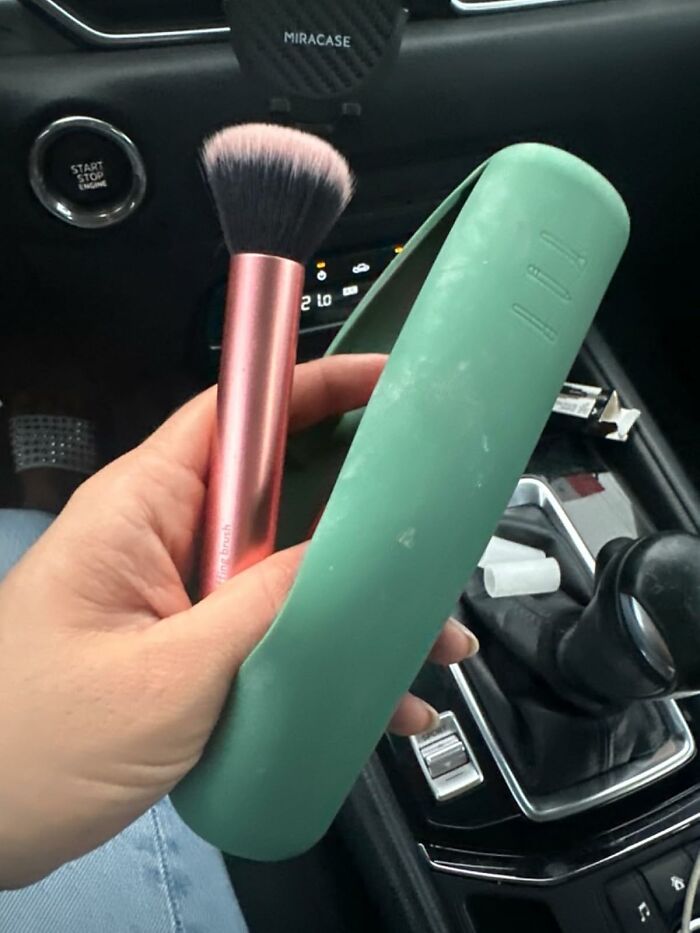 Hand holding a makeup brush and a green travel case inside a car, travel essentials for hot girl summer itinerary.