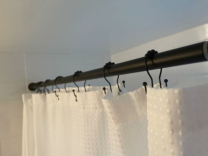 Black shower curtain rod with hooks holding a textured white shower curtain, showcasing a clever home hacks idea.